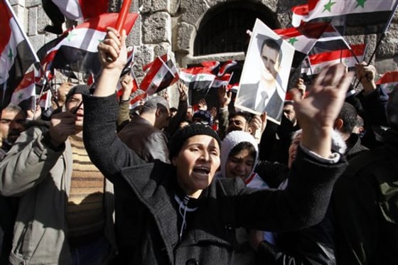 Mourners wave Syrian flags and a photo of President Bashar Assad as they chant slogans at a mass funeral Saturday for 44 people killed in twin suicide bombings that targeted intelligence agency compounds in Damascus, Syria.&nbsp; 